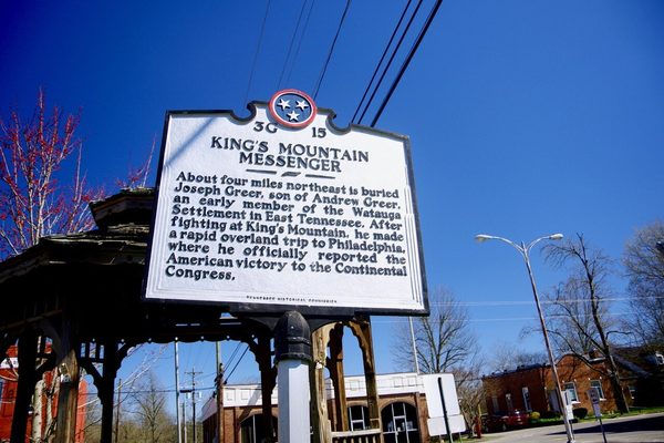 Black-and-white state historical marker titled King's Mountain Messenger beside a wooden gazebo