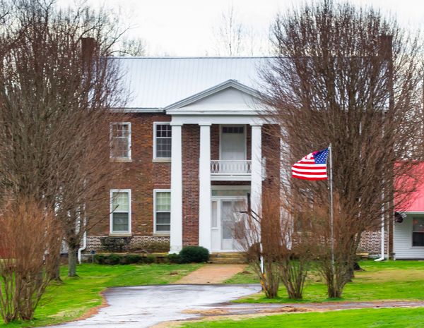 Brick house with a tall white-columned portico and an American flag in front