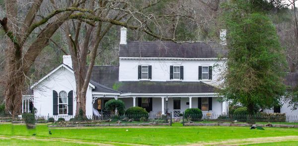 White two-story farmhouse with a porch, surrounded by trees and lawn