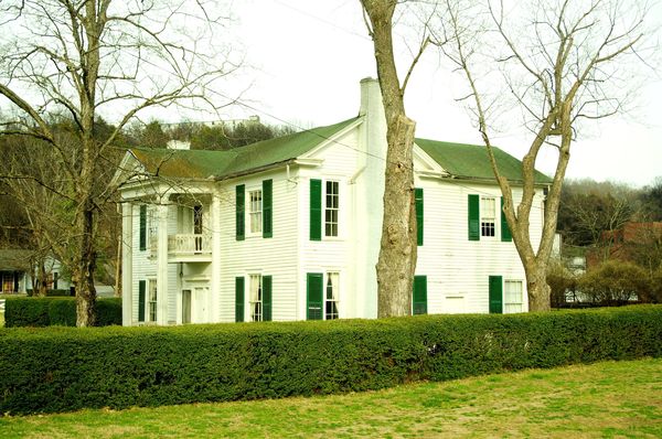 White two-story house with green shutters behind a hedge