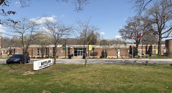 Wide view of brick college buildings across a lawn with a low sign