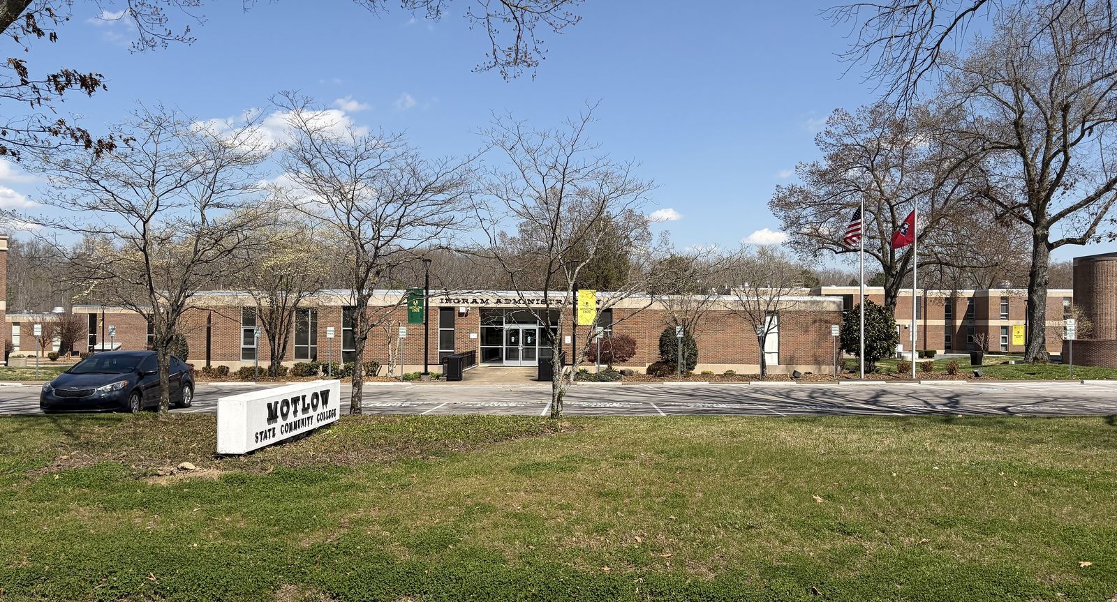 Wide view of brick college buildings across a lawn with a low sign