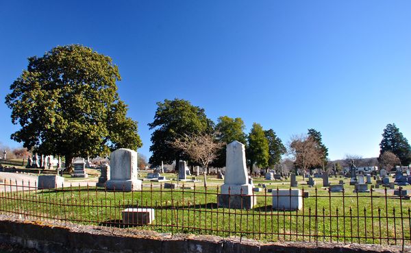 Rows of old headstones and monuments under trees behind an iron fence