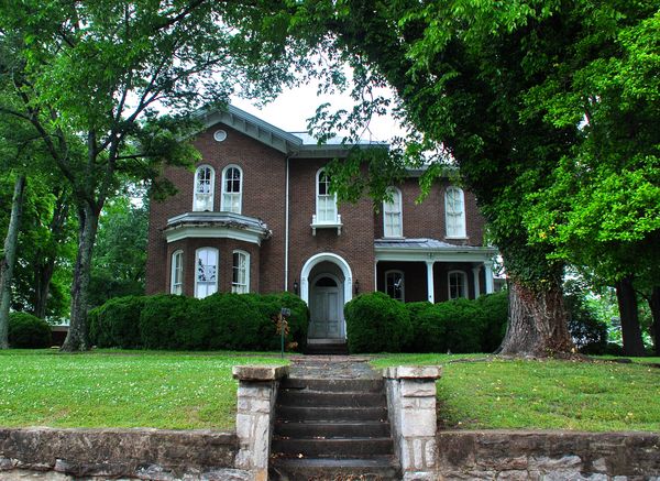 Two-story brick house with an arched entry behind stone steps