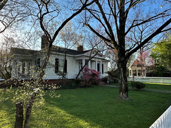 White frame house with a porch under spring trees on a residential street