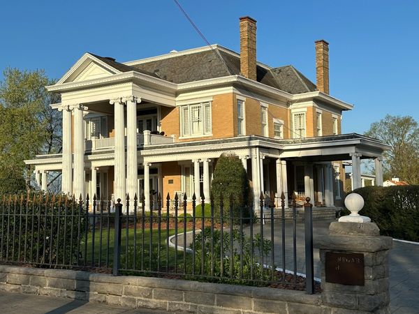Yellow brick house with tall white columns behind an iron fence