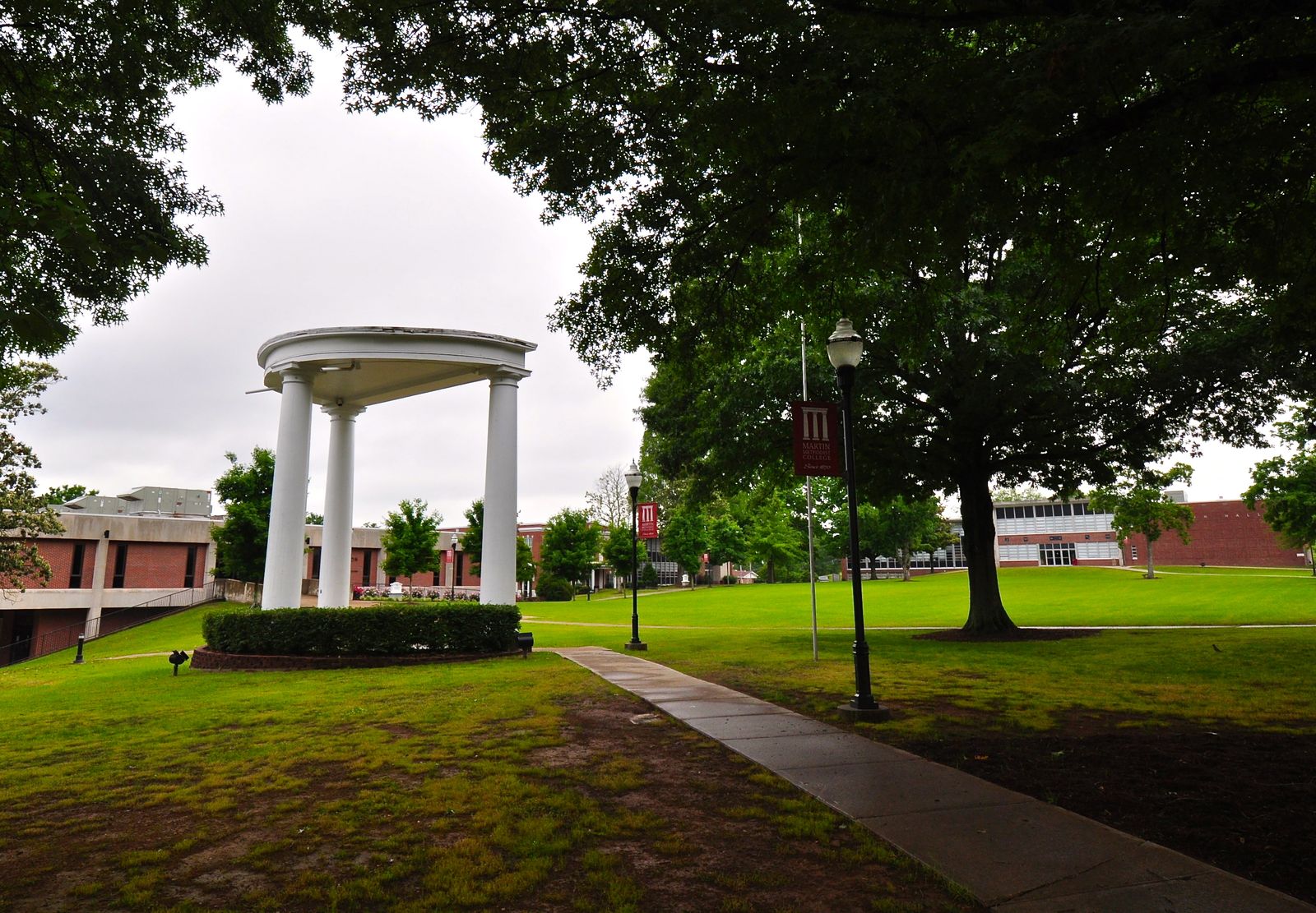 A white columned gazebo on a tree-shaded college lawn