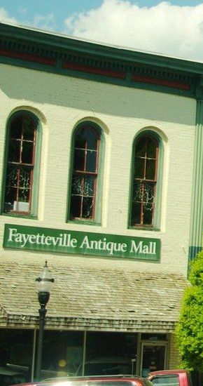 Two-story cream-painted brick storefront with three arched upper windows and a green Fayetteville Antique Mall sign over the awning, College St. E., 2015