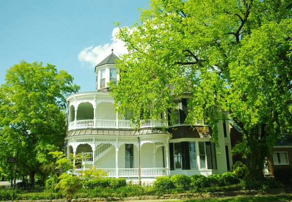 White Victorian house with a wraparound porch and turret among trees