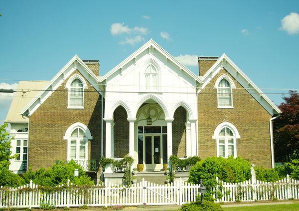 Stone Gothic Revival house with pointed gables behind a white picket fence