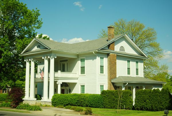 White two-story house with a columned front porch and hedges